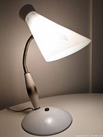 Mid century goose neck desk lamp powered on, showing light from white cone-shaped shade with geometric pattern