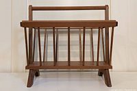 Front view of the wooden magazine rack showing the handle, vertical slats and angled legs.