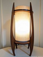 Front view of the Mid Century style table lamp lit, showing fabric shade and wooden frame with four curved legs.