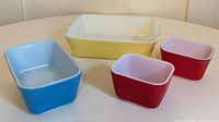 Four vintage Pyrex Fridgies containers in yellow, blue, and red colors.