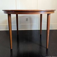 Side view of round mid-century wooden dining table with tapered legs showing its height and solid construction.