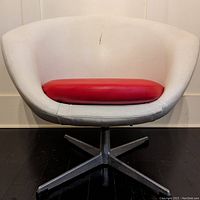 Front view of white vinyl bucket chair with red cushion on metal star swivel base, showing crack in upholstery