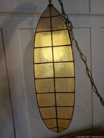 Lit elongated oval vintage swag lamp showing translucent yellow glass segments with black metal grid from a front angle