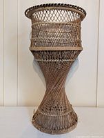 Front view of the wicker plant stand showing the hourglass body and woven lattice design
