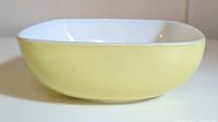 Side view of yellow Hostess Pyrex square bowl showing smooth yellow exterior and white interior