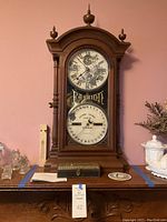Full view of Fashion calendar clock on carved furniture, rectangular wooden box at base, round bird coaster to right