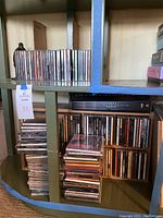 Wide view of multiple shelves filled with several rows of assorted music CDs in jewel cases, with two black CD organizers.