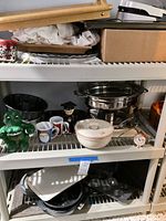 Photo of assorted kitchen items including bakeware, coffee cups, decorative figurines, stored on plastic shelving unit.