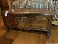 Front view of vintage cedar hope chest with carved wood design and rounded feet