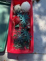 Red plastic storage container filled with blue snowflake ornaments and various Christmas light strings.