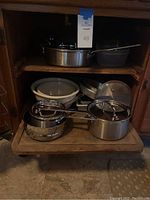 Photo showing sauce pans with lids including a large pot, multiple mixing bowls, cake pans, and plastic food storage containers all inside a cabinet.