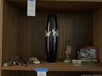 Wide shot of wood shelf with tall vase, owl figurine, framed photo, small glass hats, and carved fossils