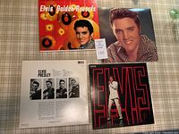 Four Elvis Presley vinyl albums arranged on a checked surface showing two album covers from front and one back cover with Elvis photos and text.