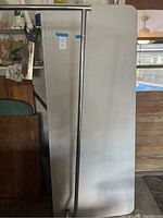 White rectangular folding table leaning vertically against wall with visible surface wear, next to metal clothes rack vertical pole.