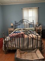 Front view of full-size gray metal bed frame with quilted striped bedding and pink throw