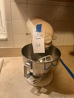 Front view of cream KitchenAid stand mixer with stainless steel bowl and attachments inside bowl, set on countertop.