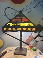 Front view of lamp illuminated showing colored glass panels with Statue of Liberty silhouette over harbor scene