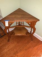 Full view of vintage oak corner table with triangular top against a wall on hardwood flooring.