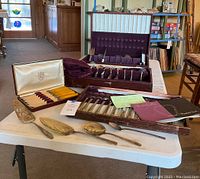 Two presentation cases on table showing yellow-handled knives, stainless flatware, loose serving pieces
