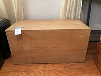 Front view of rectangular wooden toy chest with closed lid, showing surface blemishes and wear marks