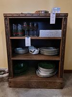 Front view of vintage wooden display shelf showing three shelves with dishes and glassware inside