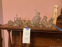 Wide view of all vintage glass figurines arranged on wooden furniture including animals, ships, and cars.