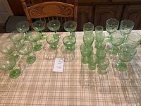 Full lot of assorted green depression glassware arranged on a table, showing glasses of different sizes and shapes.