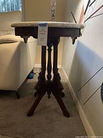 Side view of the vintage side table showing the wooden legs and carved apron supporting the marble top.