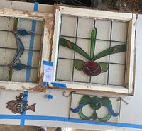 Photo showing the two framed stained glass windows with the fish and floral decorative stained glass pieces below them on a table.