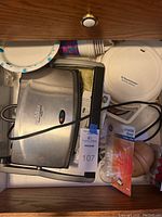 Waffle maker and panini press placed inside a drawer with lightbulb packaging visible beside them.