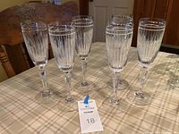 Set of six Waterford champagne flutes arranged on a beige plaid tablecloth, showing full view of all glasses to capture the set and etching details.
