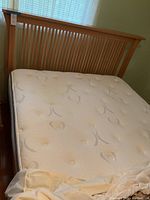 View of the queen mattress and wooden mission style bed headboard showing floral patterned tufted mattress surface and slatted wood headboard design.