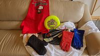 Full lot displayed on couch including red apron, yellow frisbee, gloves, oven mitt, and cooking utensils