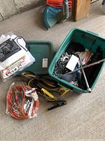 Photo of the green plastic bin containing a metal tow chain with hooks, ropes, and automotive cables including yellow ones and black clamps, also including parts of other items around it.