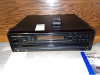 Front view of black Onkyo Integra DX-C909 6-disc CD player with remote and user manual on wooden surface.