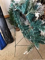 Photo of artificial Christmas wreath mounted on green metal tripod stand, showing construction and support apparatus.