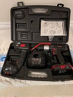 Opened black plastic carry case containing a cordless work light, charger, instruction manual, and space for a drill and battery.