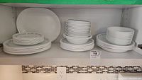 Wide view of all dishware items on shelves including stacked dinner plates, salad plates, bowls, and serving platter.