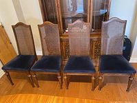 Four vintage dining chairs in front of a wooden cabinet, showing cane back and navy velvet seat upholstery