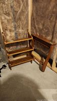 Two maple Colonial-style display shelves in a storage room with a backdrop of insulation and a plastic sheet. Left shelf has three shelves, right one has rung design.