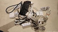 Assortment of power bars, extension cords, and multiple plug wall outlet adapters all coiled and piled together on carpeted floor.