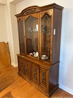 Front view of the solid wood vintage hutch showing three glass doors on the top display cabinet and four bifold carved wooden doors at the base.