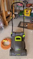 Image showing full view of LawnMaster electric lawn mower with folded handle and orange extension cord coiled beside it.