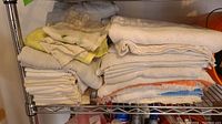 Folded shop rags and towels in various colors, stacked on a metal wire shelf.