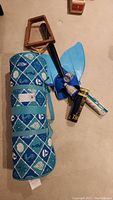 Photo of rolled beach mat with ocean themed design, two wooden badminton rackets and a blue mermaid tail fin accessory laying on floor.