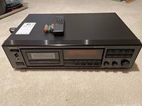 Front view of the Onkyo tape deck with remote and batteries on top.