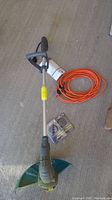 Full view of Yardworks electric string trimmer with orange extension cord and two extra spools on concrete floor.