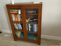 Front view of the solid wood cabinet bookcase with glass doors and visible shelves stocked with books.