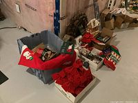 Photo showing red Christmas stockings with snowmen and holiday text, red fabric bows, a box with Christmas decorations on a basement floor.