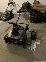 Full view of snow blower with charger, batteries and manuals arranged on the floor